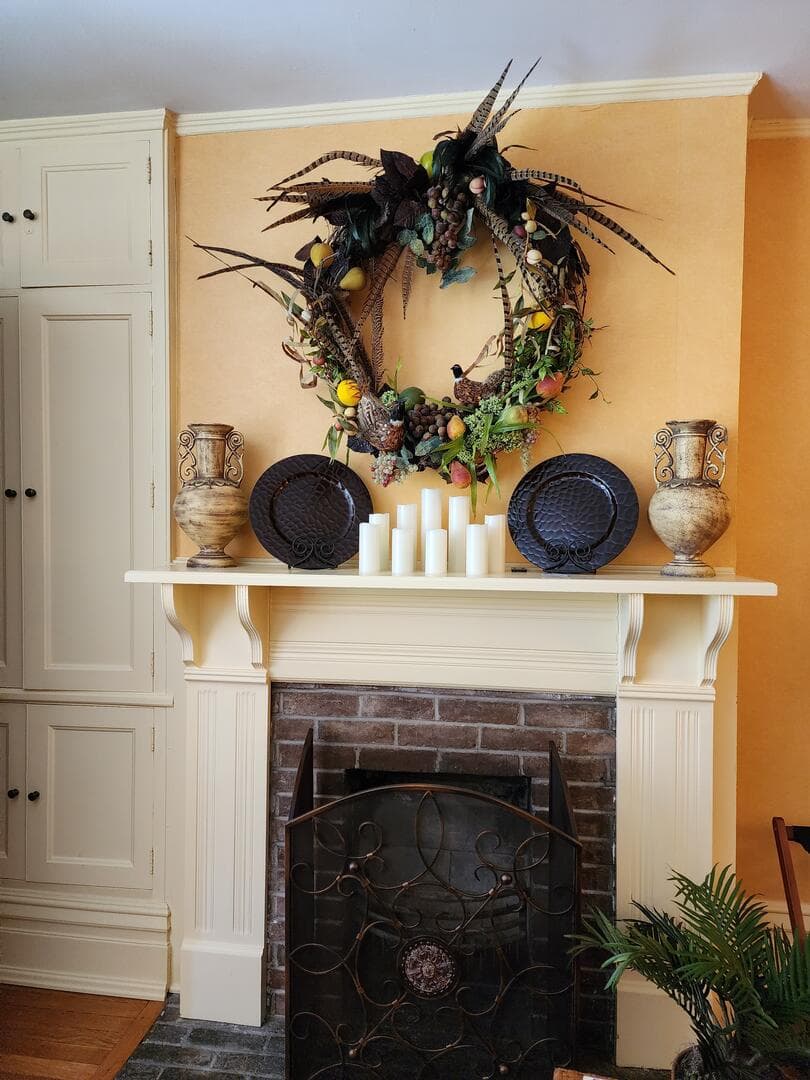 A cozy fireplace mantel adorned with a decorative wreath, candles, and ornate vases.