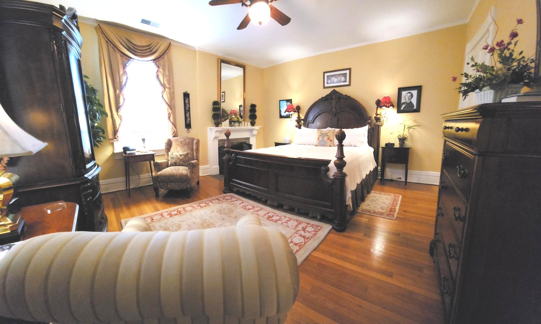 A cozy, elegantly decorated bedroom featuring a wooden bed, armchair, and warm yellow walls.