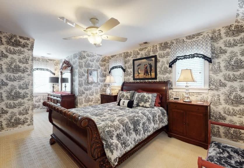 A cozy bedroom featuring a patterned wallpaper, a large bed with a quilt, and wooden furniture.