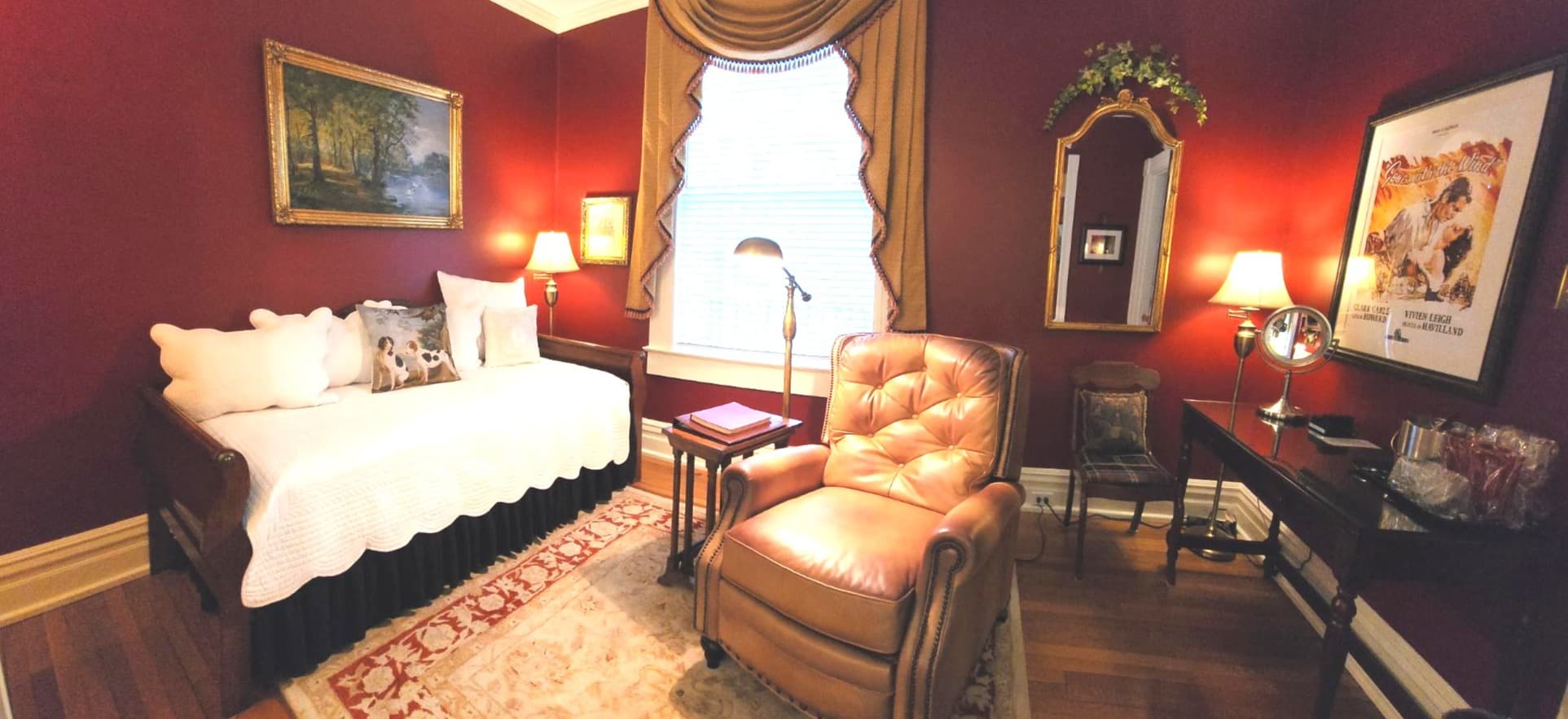 Cozy room with a red wall, a daybed, a reading chair, a small table, and decorative wall art.