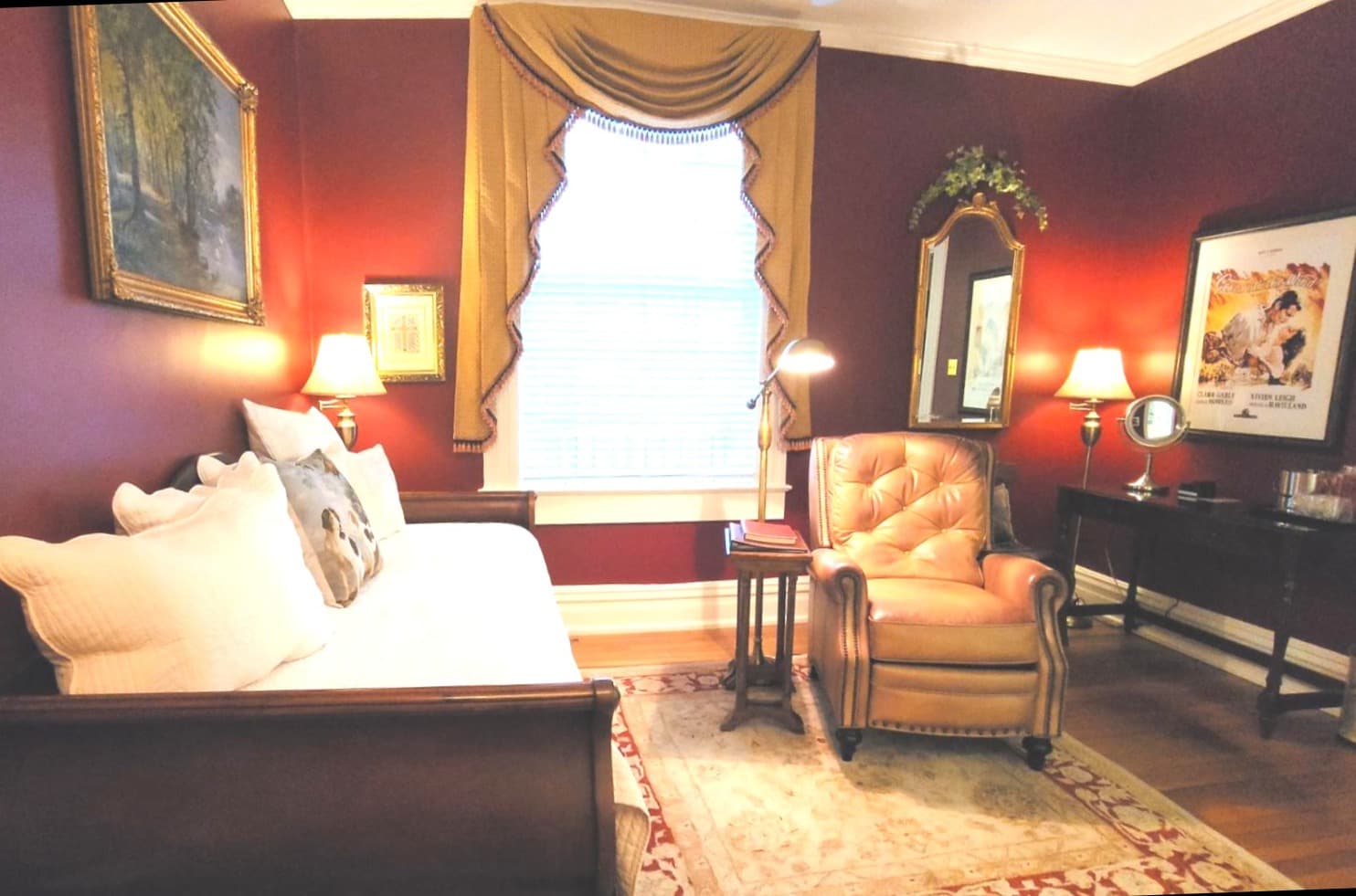 A cozy reading nook featuring a white daybed, a brown leather armchair, and warm decorative accents against a rich red wall.