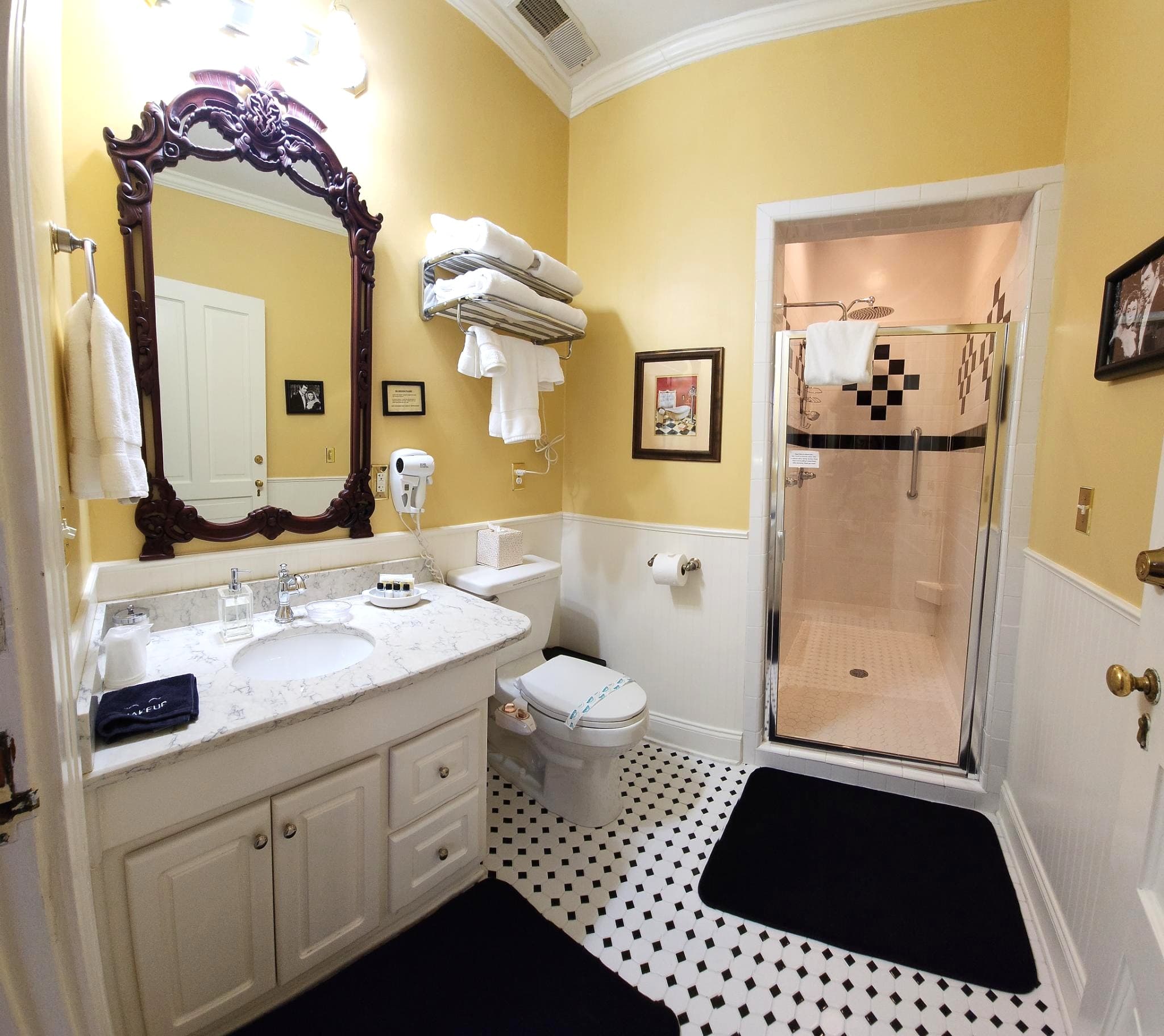 A stylish bathroom featuring a marble sink, a large mirror, black and white tiled floor, and a glass shower enclosure.