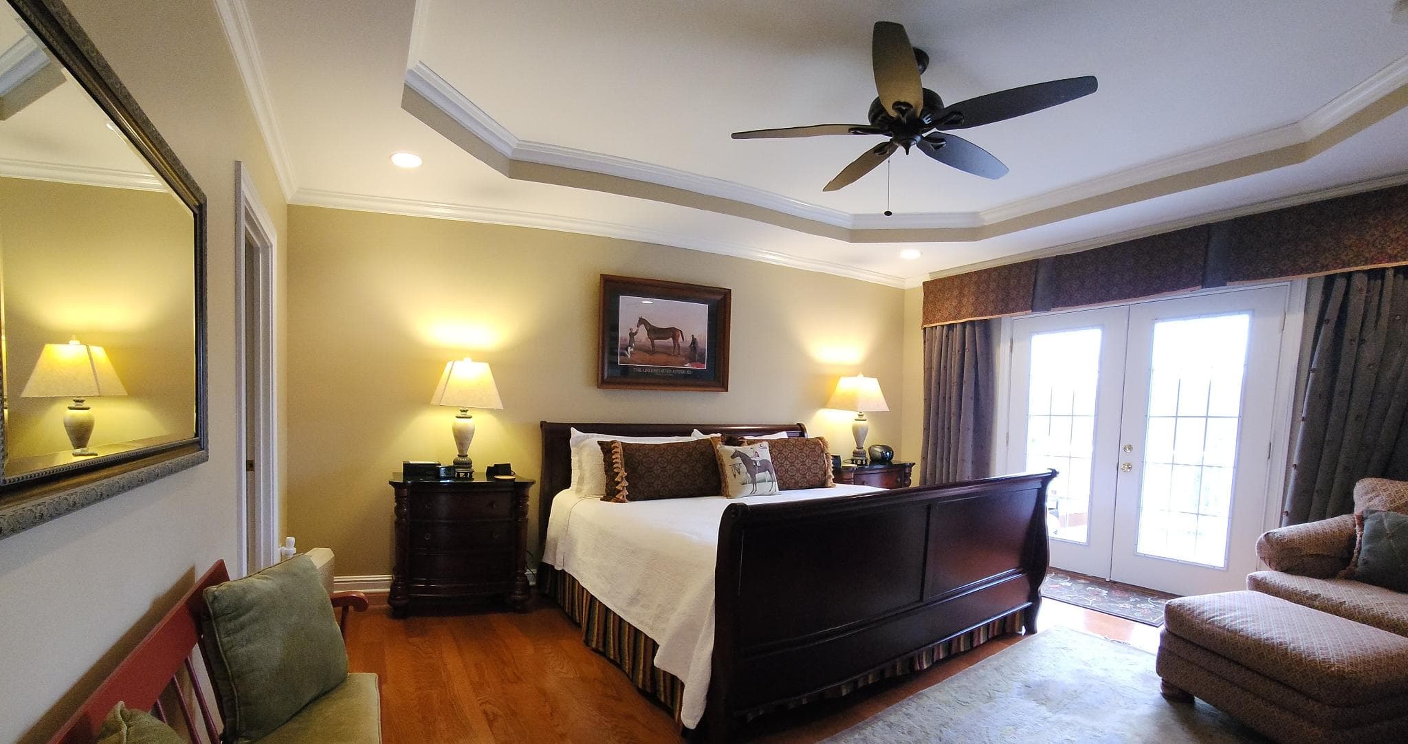 A cozy bedroom featuring a king-sized bed, two lamps, a painting, and a view of double doors leading outside.