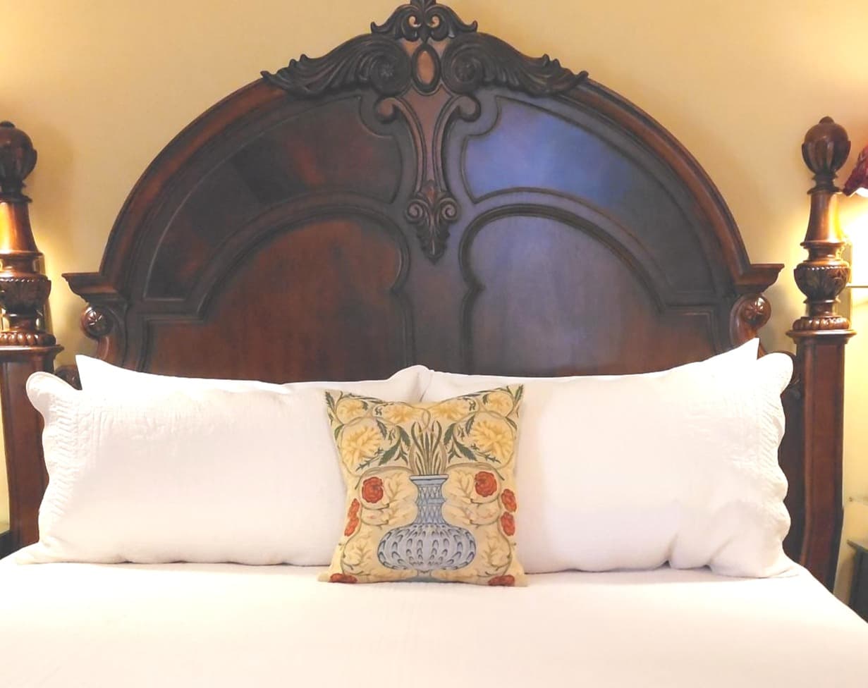 A bed with a wooden headboard and decorative pillows, including a floral accent pillow at the center.