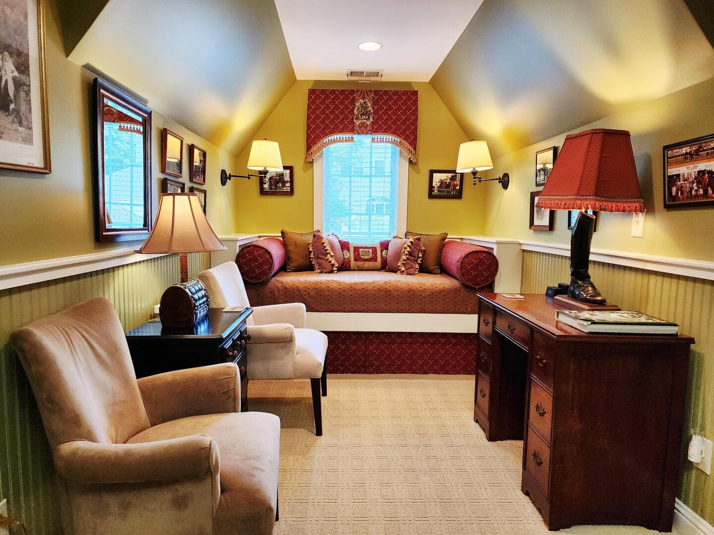 A cozy reading nook with a daybed, two armchairs, a desk, and soft lighting in a warmly colored room.
