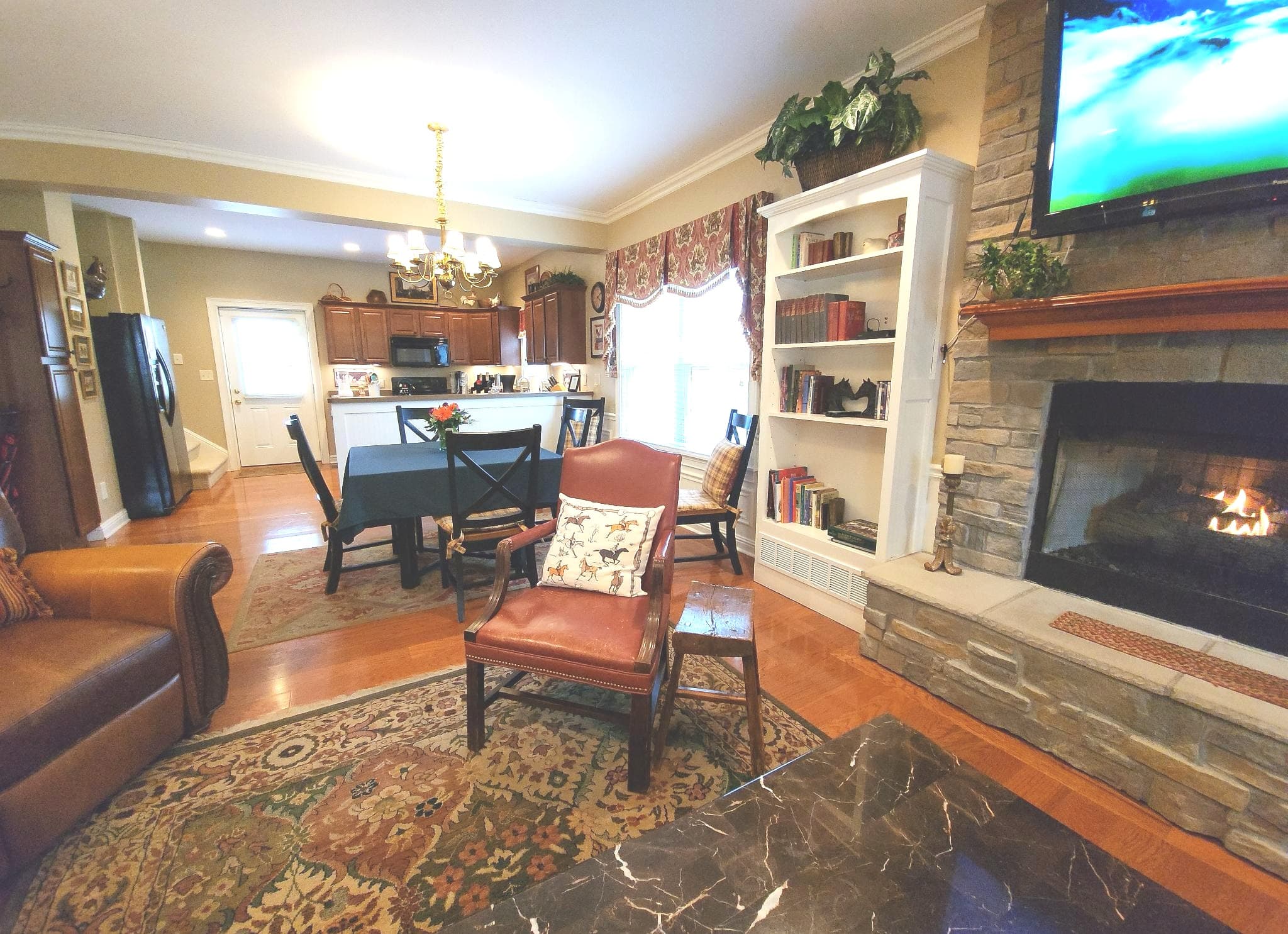 Cozy living room featuring a fireplace, bookshelves, and a view of the kitchen.