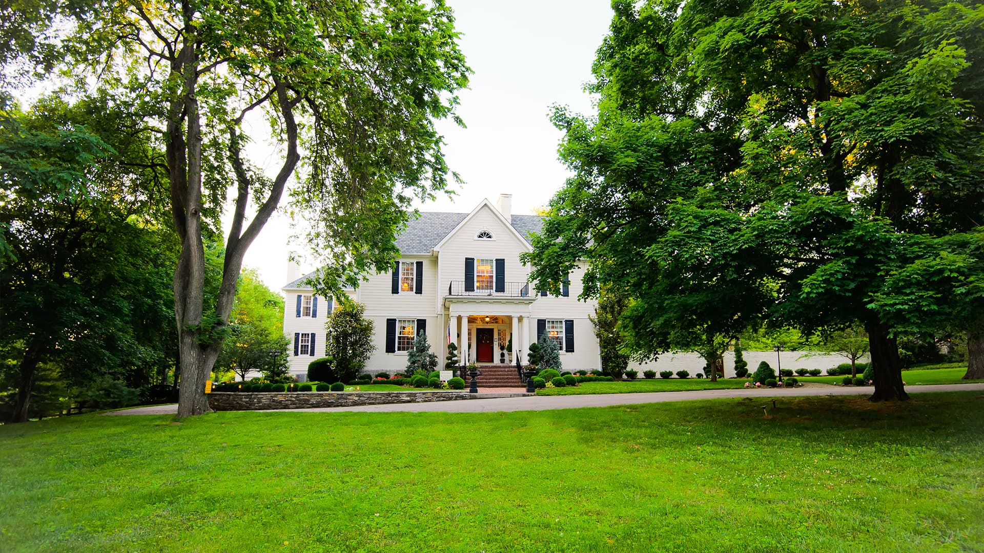A large white house surrounded by lush green trees and a well-manicured lawn.