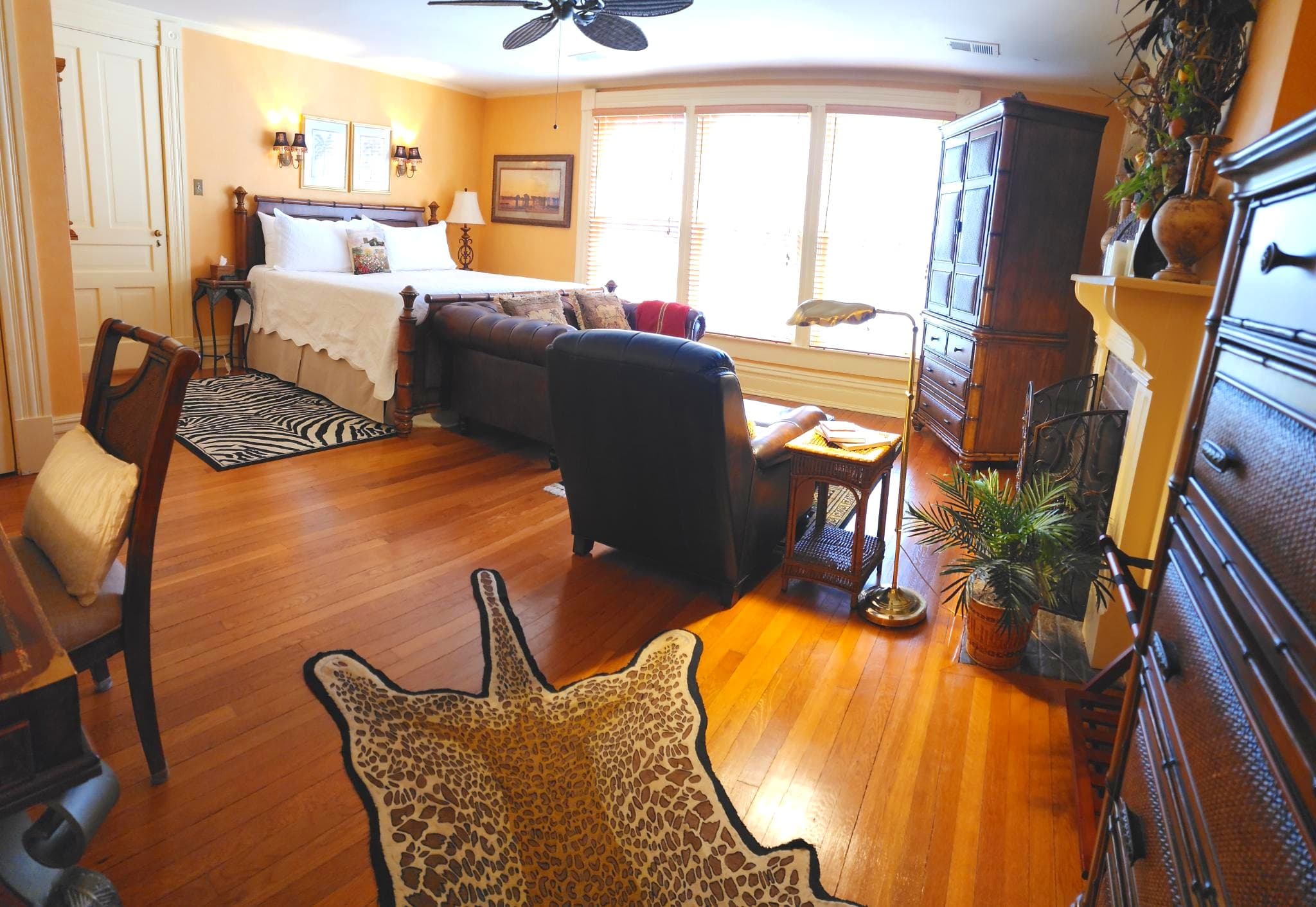 A cozy bedroom with wooden floors, a large bed, comfortable seating, and ample natural light.