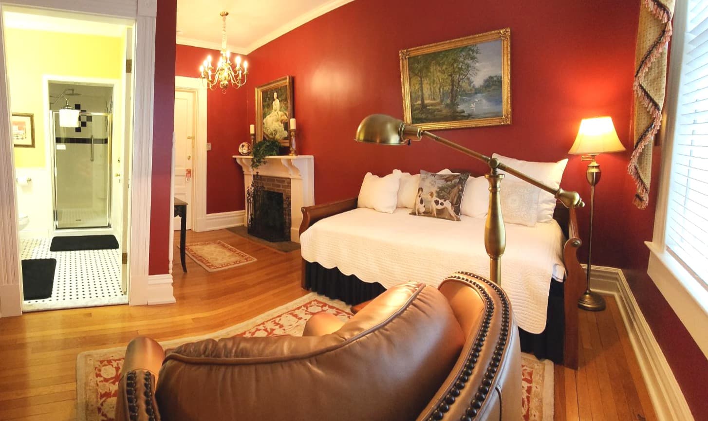 Cozy bedroom with a daybed, antique furnishings, and an adjoining bathroom, set against rich red walls.