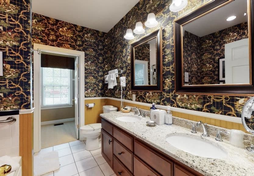 A stylish bathroom featuring a dual vanity, ornate wallpaper, and large mirrors.