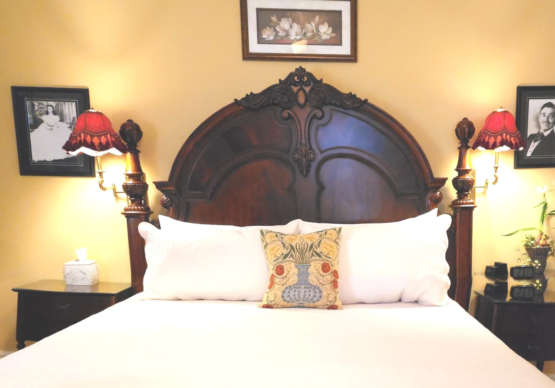 A cozy bedroom featuring a wooden bed frame, decorative pillows, bedside lamps, and framed photos on the wall.