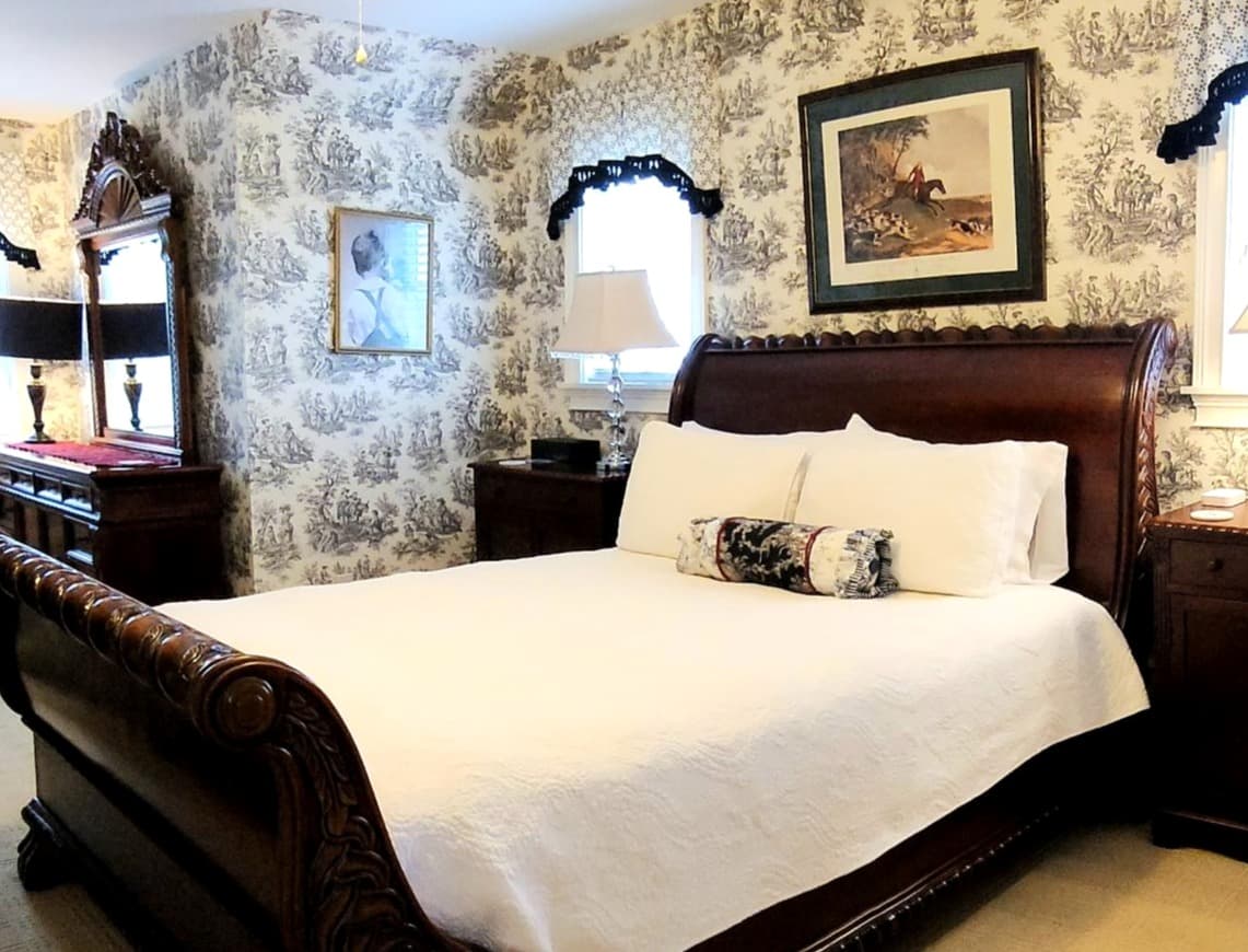 A cozy bedroom featuring a large wooden sleigh bed, patterned wallpaper, and framed artwork.