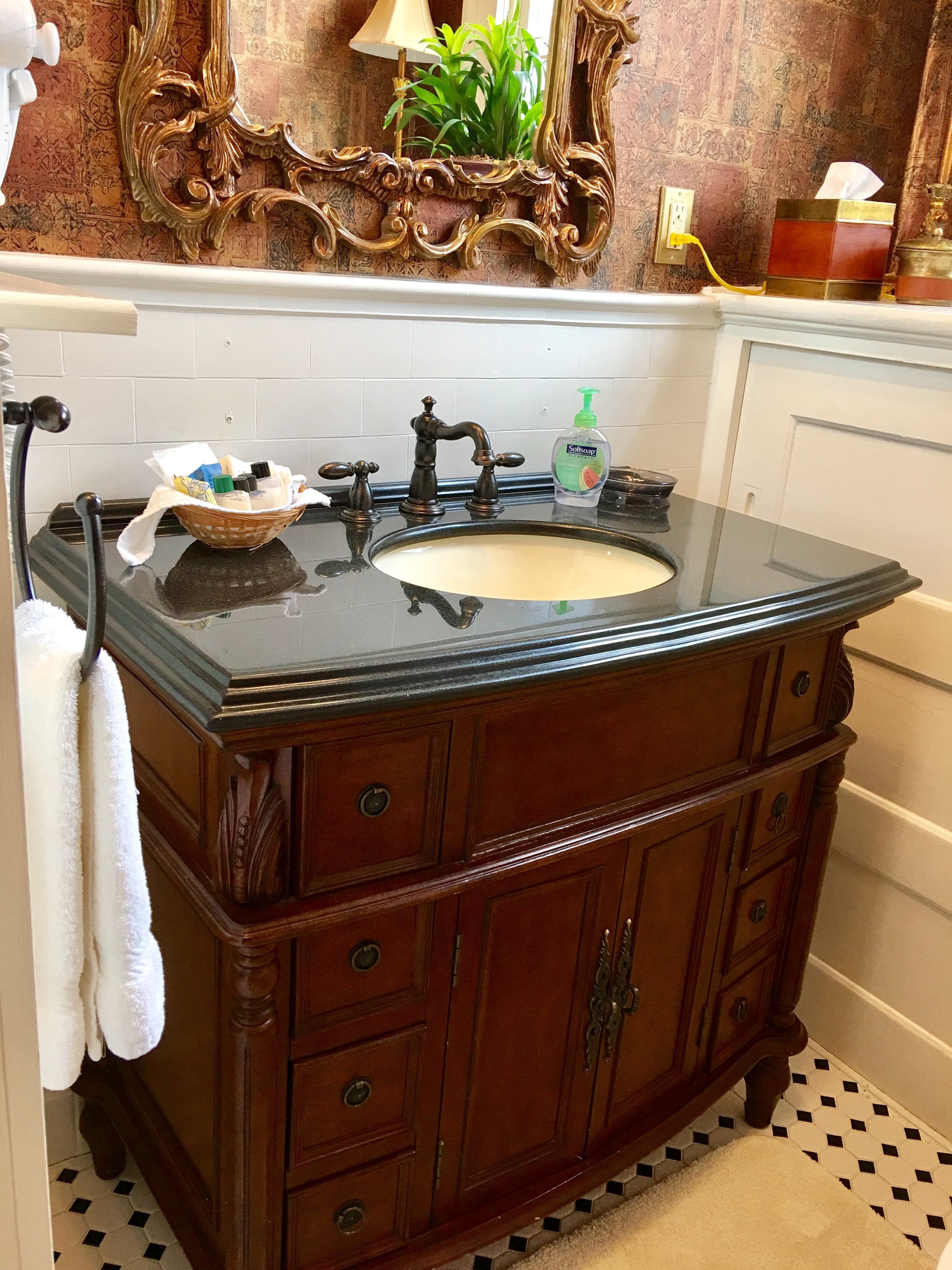 A wooden bathroom vanity with a black countertop, sink, and decorative mirror above.