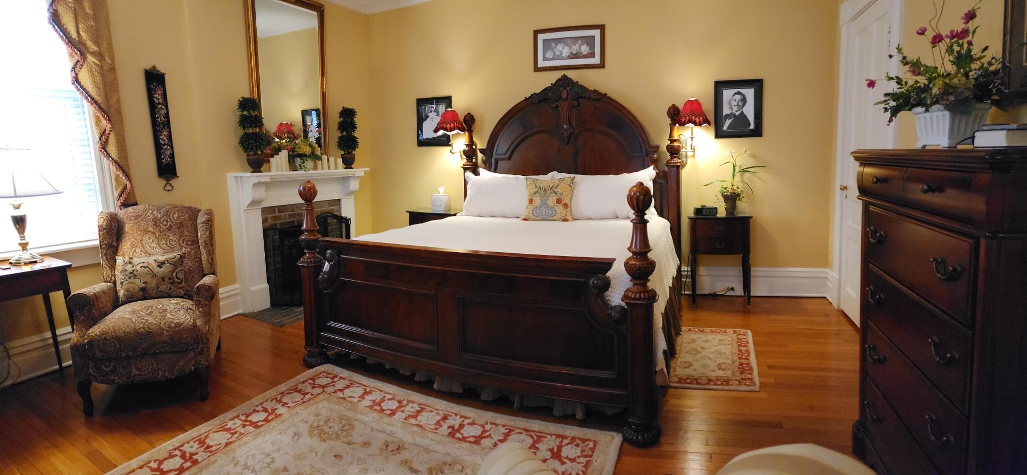 Cozy bedroom featuring a wooden bed, armchair, and decorative accents against a warm yellow wall.
