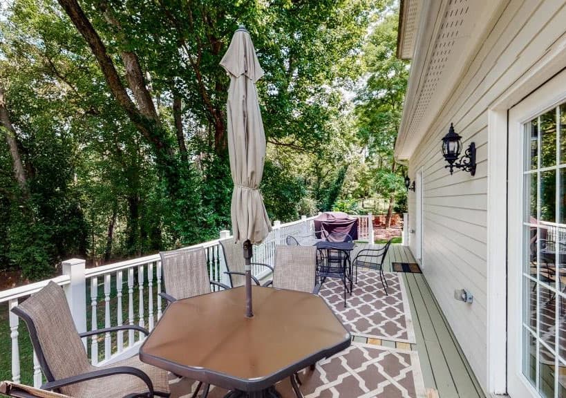 A deck with an octagonal table, chairs, and a patio umbrella surrounded by trees.