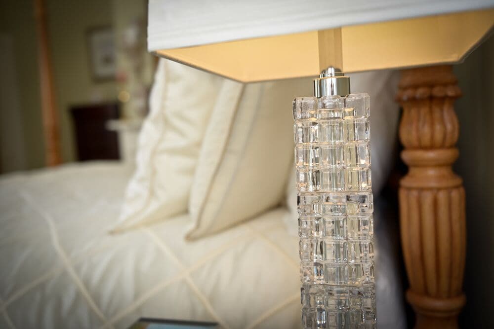 Close-up of a crystal lamp base next to a neatly made bed with white linens.