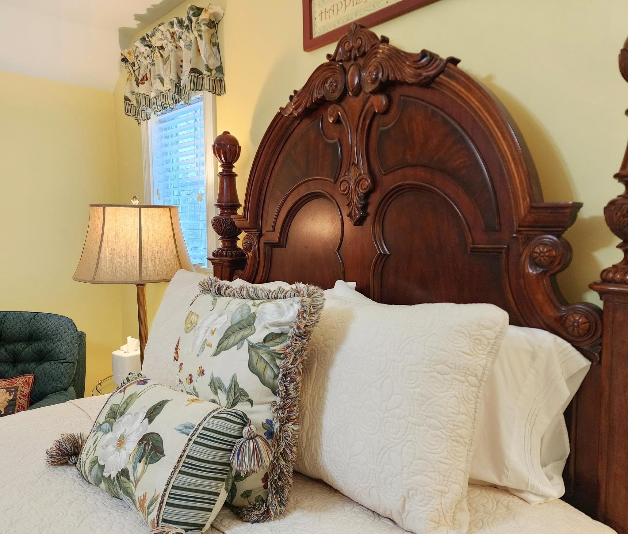 A cozy bedroom with a wooden headboard, decorative pillows, a lamp, and soft yellow walls.